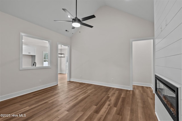 unfurnished living room with high vaulted ceiling, a large fireplace, a ceiling fan, and wood finished floors