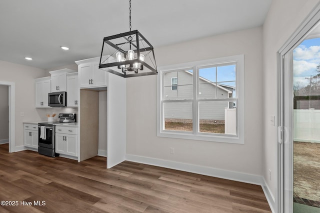 kitchen featuring dark wood-style floors, baseboards, stainless steel appliances, white cabinets, and a chandelier