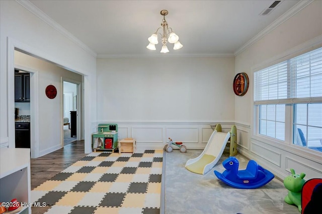 rec room with visible vents, crown molding, wood finished floors, a notable chandelier, and a decorative wall