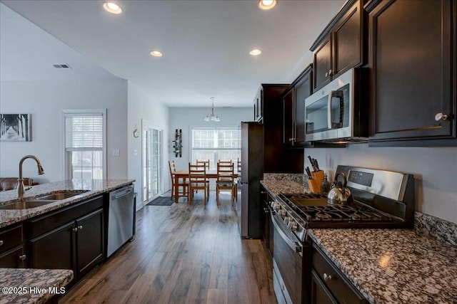 kitchen featuring visible vents, dark wood-type flooring, dark stone countertops, appliances with stainless steel finishes, and a sink