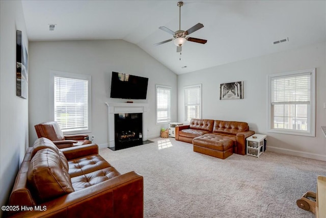 carpeted living room featuring baseboards, visible vents, lofted ceiling, a fireplace with flush hearth, and ceiling fan