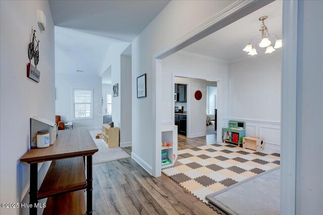 hallway featuring wood finished floors, baseboards, an inviting chandelier, ornamental molding, and a decorative wall