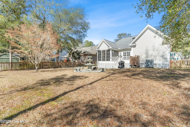 rear view of property with central air condition unit, a lawn, fence private yard, and a sunroom