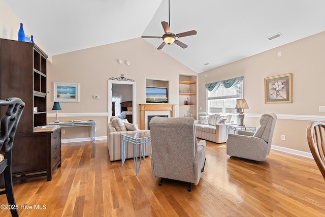 living room with light wood finished floors, visible vents, ceiling fan, built in features, and a fireplace