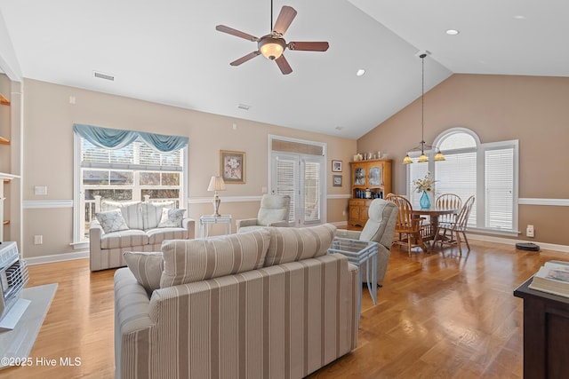 living area with visible vents, ceiling fan with notable chandelier, light wood-style flooring, and vaulted ceiling