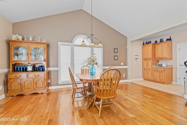 dining area with baseboards, light wood-style floors, and high vaulted ceiling