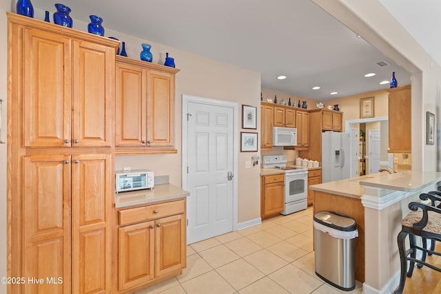 kitchen with white appliances, a breakfast bar area, light tile patterned floors, a sink, and light countertops