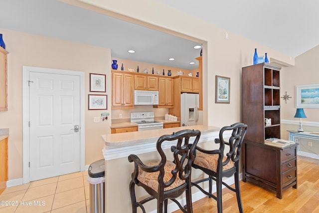 kitchen featuring a breakfast bar, light brown cabinets, recessed lighting, white appliances, and light countertops