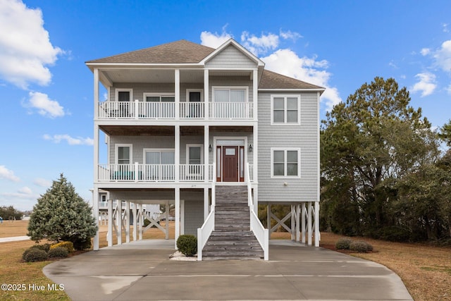 coastal inspired home featuring a shingled roof, a porch, stairs, a carport, and driveway