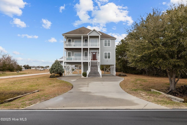 beach home with a balcony, concrete driveway, a front yard, a carport, and stairs