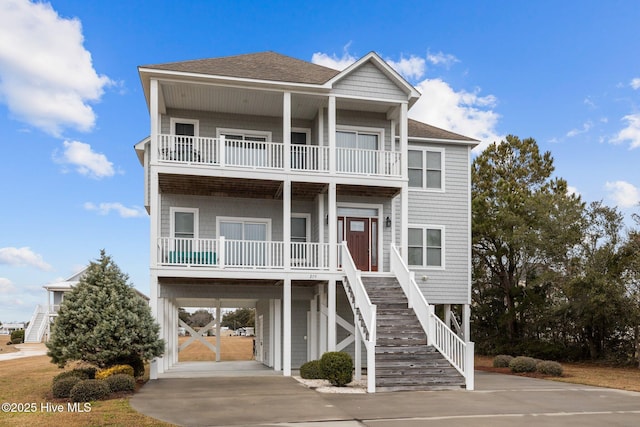 raised beach house featuring a carport, stairway, driveway, and a shingled roof