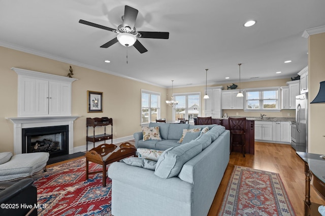 living room featuring a glass covered fireplace, a wealth of natural light, light wood-style flooring, and ornamental molding