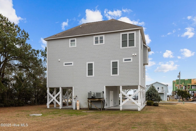 rear view of property with central AC unit, a yard, and roof with shingles