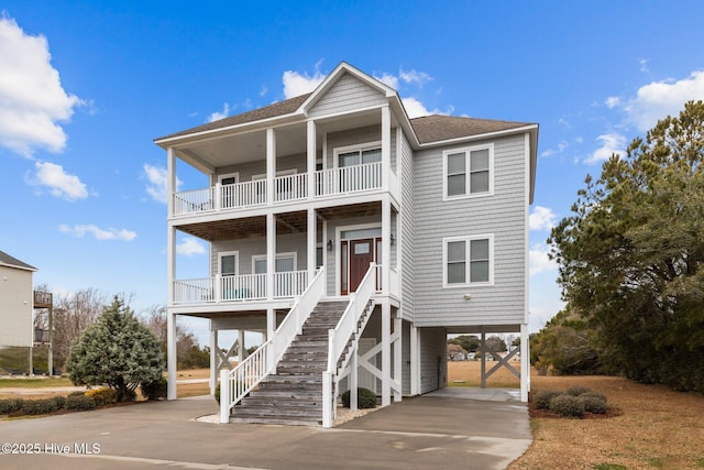 beach home with a balcony, driveway, roof with shingles, covered porch, and a carport