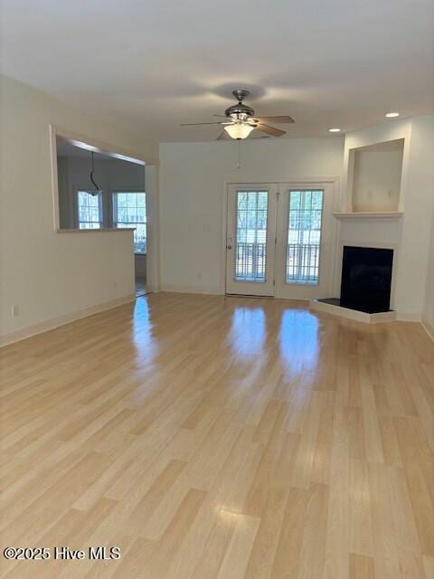 unfurnished living room featuring a fireplace with raised hearth, a healthy amount of sunlight, light wood-type flooring, and ceiling fan