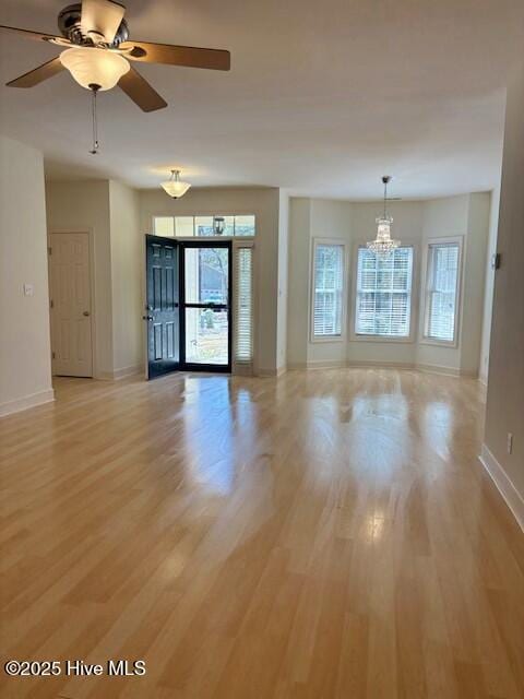 empty room featuring ceiling fan with notable chandelier, baseboards, and light wood finished floors