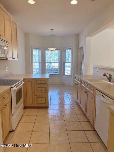 kitchen featuring light tile patterned floors, white appliances, a peninsula, and a sink