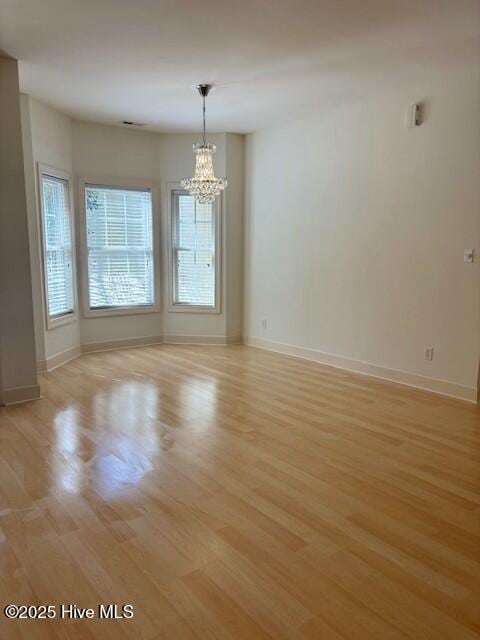 unfurnished room featuring light wood-style floors, baseboards, and a chandelier