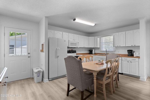 109 NE 17th St, Oak Island, NC 28465 - kitchen with white appliances, a sink, light wood-style flooring, white cabinets, and a textured ceiling