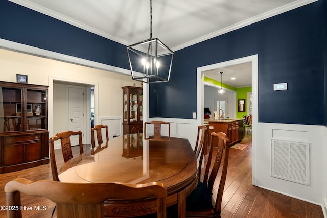 dining room featuring visible vents, ornamental molding, wood-type flooring, wainscoting, and a decorative wall