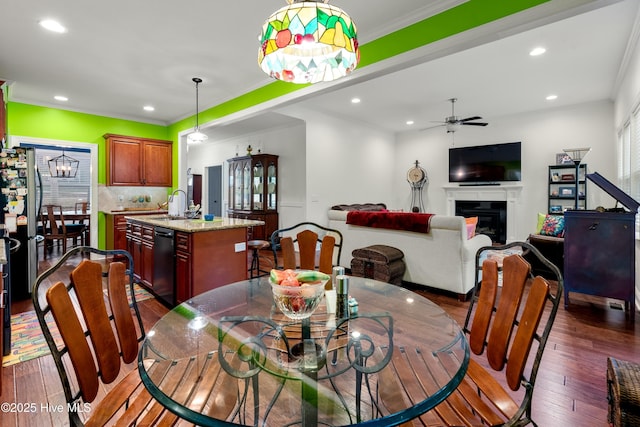 dining room featuring a glass covered fireplace, ornamental molding, ceiling fan, and dark wood-style flooring