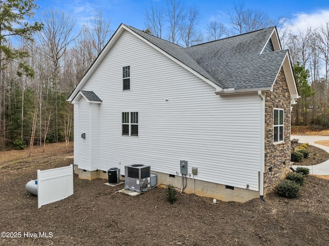 view of home's exterior with a shingled roof, central air condition unit, stone siding, and crawl space