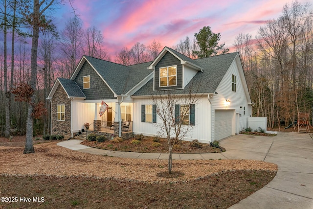 view of front of house with driveway, roof with shingles, a porch, stone siding, and a garage