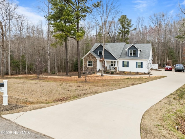 view of front facade with stone siding, a porch, a forest view, and driveway