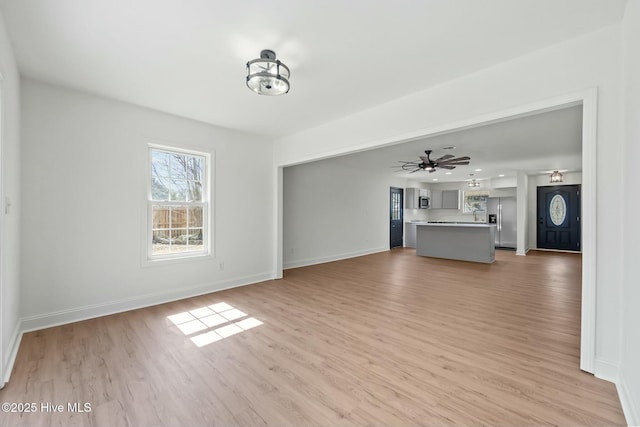 unfurnished living room featuring ceiling fan, light wood-type flooring, and baseboards