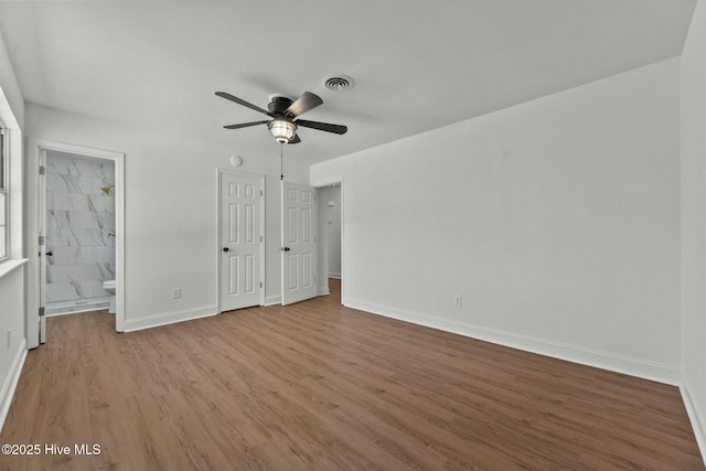 unfurnished bedroom featuring visible vents, ceiling fan, baseboards, wood finished floors, and ensuite bath