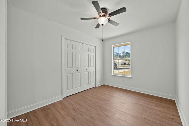 unfurnished bedroom featuring ceiling fan, wood finished floors, a closet, and baseboards