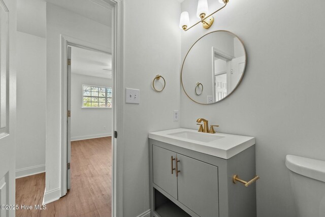 half bathroom featuring vanity, toilet, wood finished floors, and baseboards