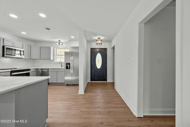 kitchen featuring light wood-style flooring, gray cabinets, recessed lighting, stainless steel appliances, and baseboards