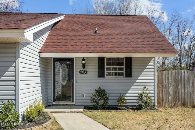 view of exterior entry with fence and roof with shingles