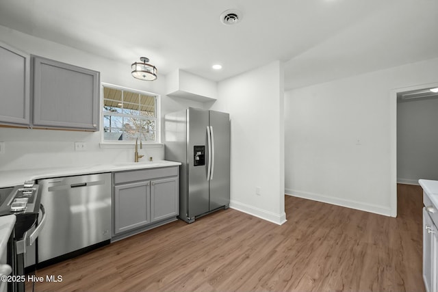 kitchen featuring gray cabinetry, a sink, stainless steel appliances, light wood-style floors, and baseboards