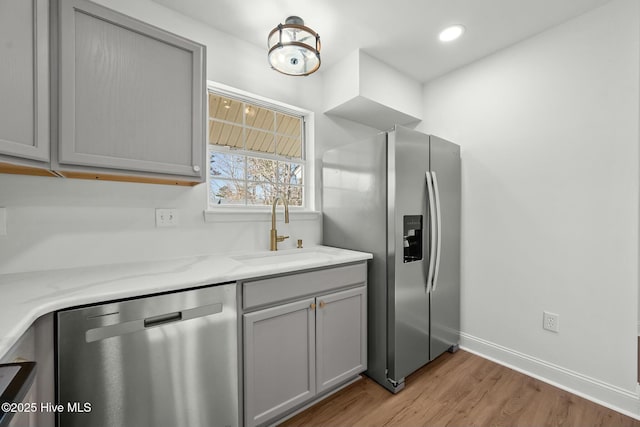 kitchen with light wood finished floors, baseboards, gray cabinets, stainless steel appliances, and a sink