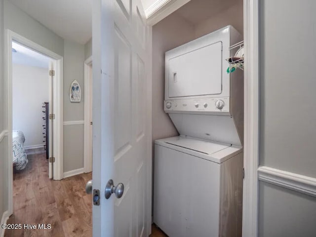 laundry room featuring laundry area, wood finished floors, baseboards, and stacked washing maching and dryer