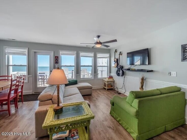 living area with wood finished floors, a healthy amount of sunlight, a wainscoted wall, and ceiling fan