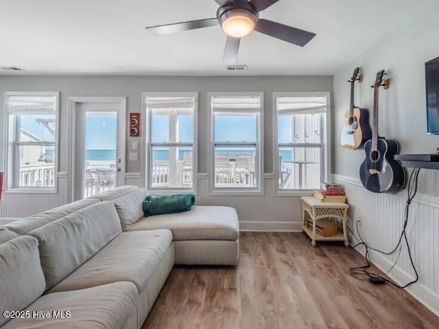 living area featuring visible vents, ceiling fan, light wood-style floors, and a wainscoted wall