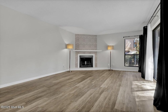 unfurnished living room featuring a large fireplace, baseboards, and light wood-style flooring