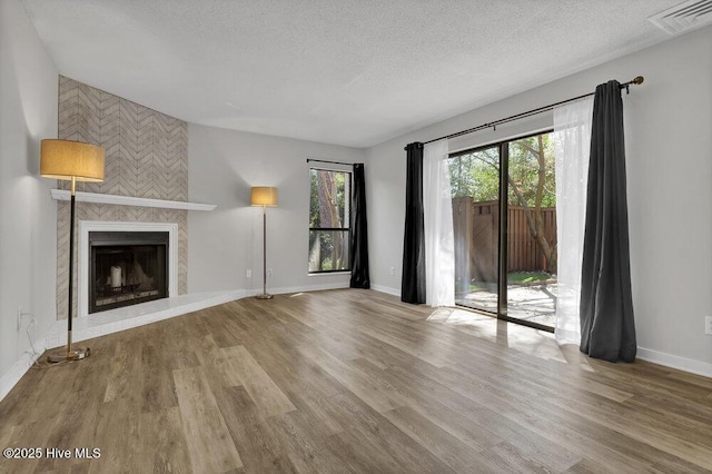 unfurnished living room featuring wood finished floors, baseboards, visible vents, a fireplace, and a textured ceiling