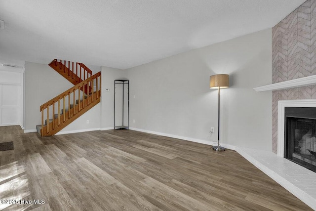 unfurnished living room with a fireplace, stairway, wood finished floors, and baseboards