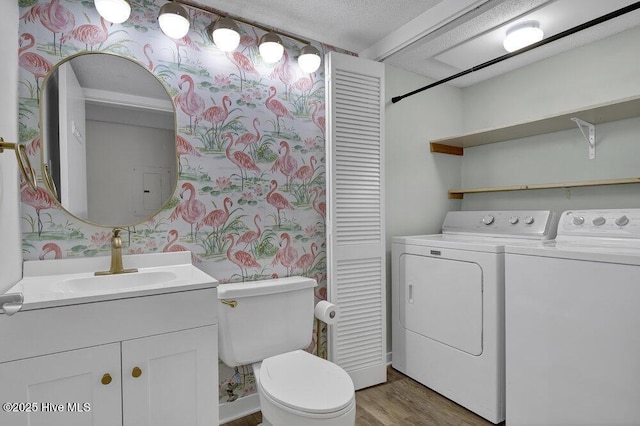 bathroom with washing machine and clothes dryer, toilet, wallpapered walls, and wood finished floors