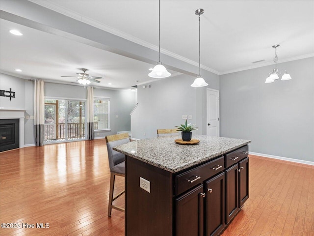 kitchen with light wood-style flooring, a kitchen breakfast bar, open floor plan, hanging light fixtures, and ornamental molding