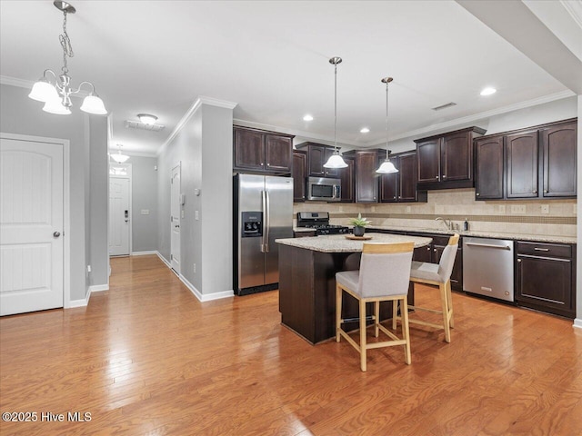 kitchen featuring appliances with stainless steel finishes, dark brown cabinets, crown molding, decorative backsplash, and a breakfast bar area