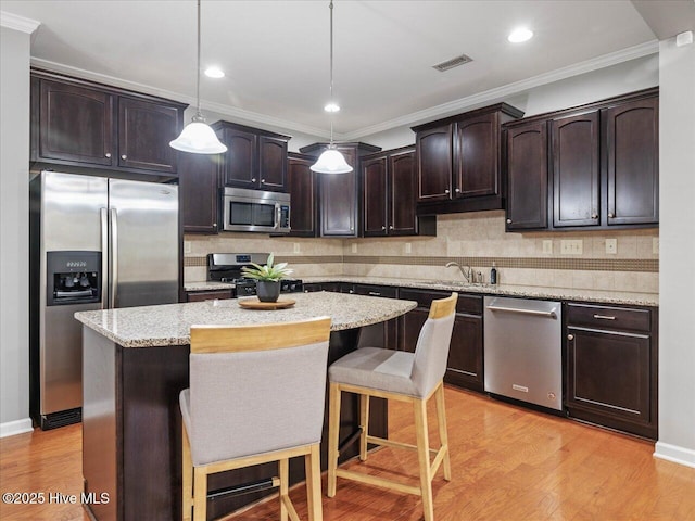 kitchen with stainless steel appliances, dark brown cabinetry, a center island, decorative backsplash, and light wood finished floors
