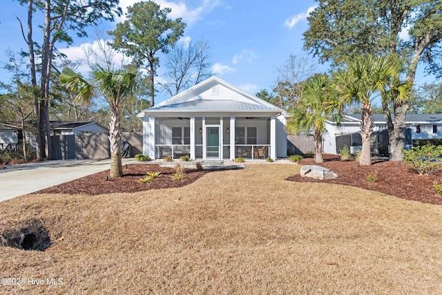 view of front of home featuring a front lawn, fence, concrete driveway, metal roof, and a sunroom