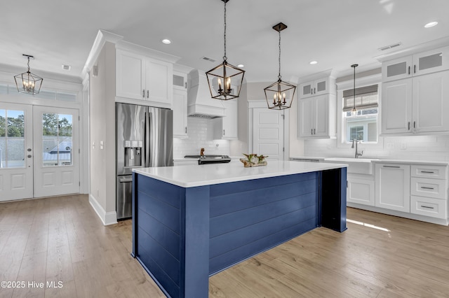 kitchen featuring stainless steel appliances, white cabinetry, a notable chandelier, and custom range hood