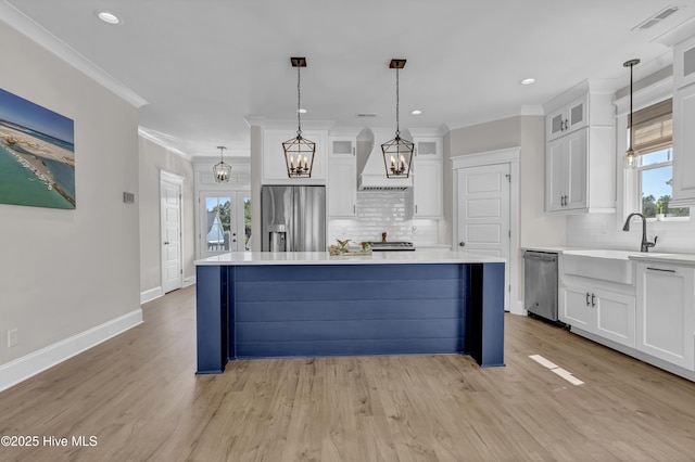 kitchen with stainless steel appliances, white cabinetry, a kitchen island, and custom range hood