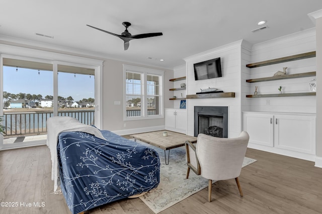 living area with visible vents, a fireplace, a ceiling fan, and crown molding